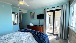 A bedroom with a bed, a dresser, a ceiling fan, a TV, and a sliding glass door leading to a balcony. - Ocean Forest Villas by Palmetto Vacations (Myrtle Beach)