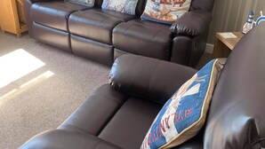 A brown leather sofa with three decorative pillows, one with a lighthouse design and another with a beach theme.