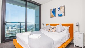 Une chambre d’hôtel moderne avec un grand lit, une table de chevet, une porte vitrée donnant sur un balcon et deux tableaux abstraits accrochés au mur.