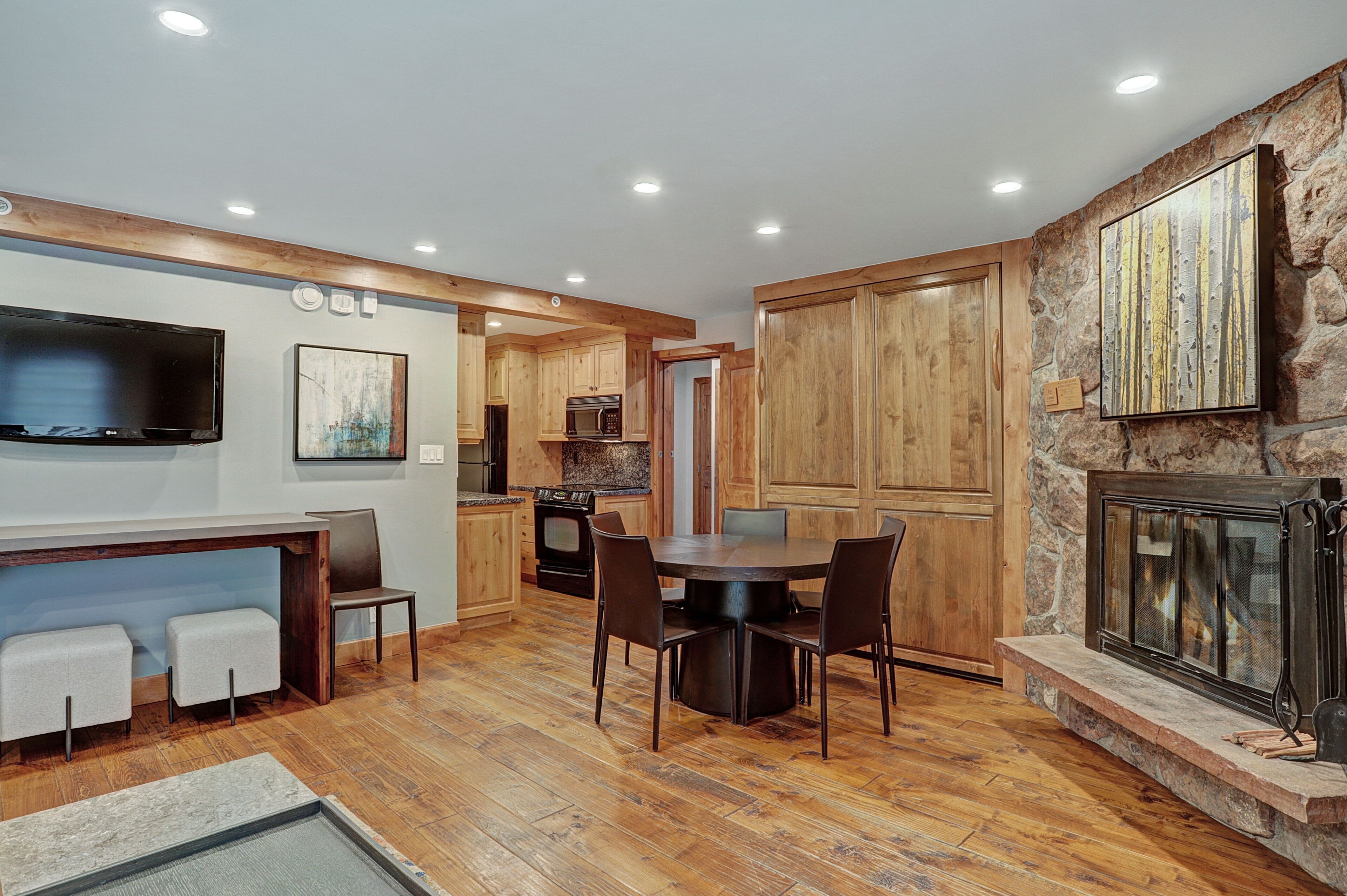 A modern kitchen with wooden cabinets, a dining area with a round table, and a stone fireplace.