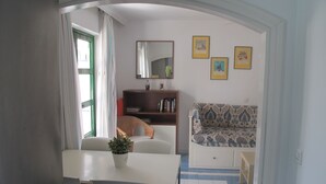 Ein gemütlicher Wohnraum mit Esstisch, Stühlen, einer Couch, einem Bücherregal und einem Spiegel.