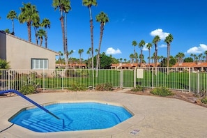 A swimming pool with a blue deck, surrounded by a fence and palm trees.