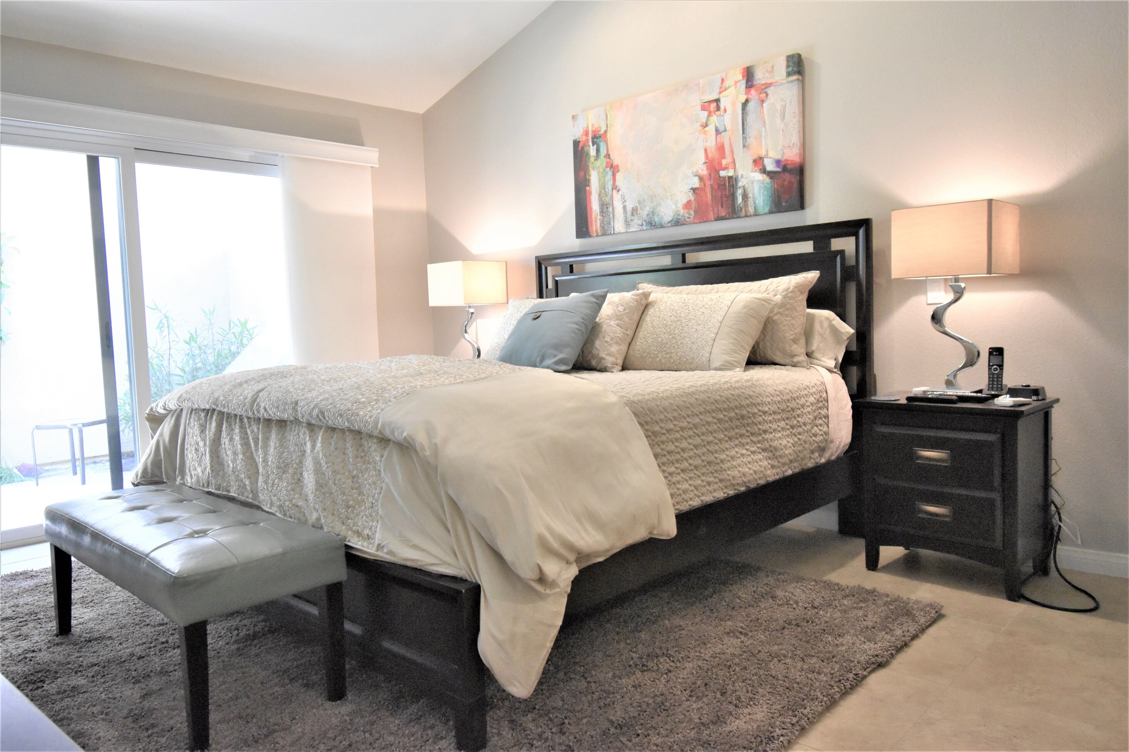 A bedroom with a large bed, a bench, a nightstand, and a painting on the wall.