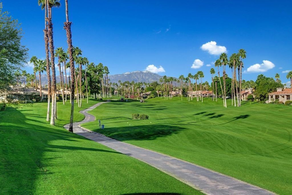 Un campo de golf con un camino despejado, palmeras y una montaña al fondo.