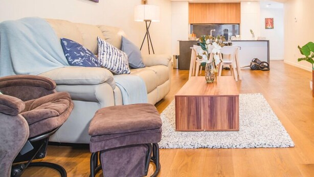 A modern living room with a sofa, ottoman, and coffee table, a dining area with chairs, a kitchen in the background, and a painting on the wall. - Modern 2bed2bath APT at Neutral Bayparking+wifi (Neutral Bay)