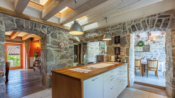 A kitchen with stone walls, wooden beams, and a central island with a light-colored countertop. - House Carpe Diem (Jurdani)