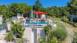 A pool area with chairs and a table, surrounded by greenery and a stone wall. - House Carpe Diem (Jurdani)