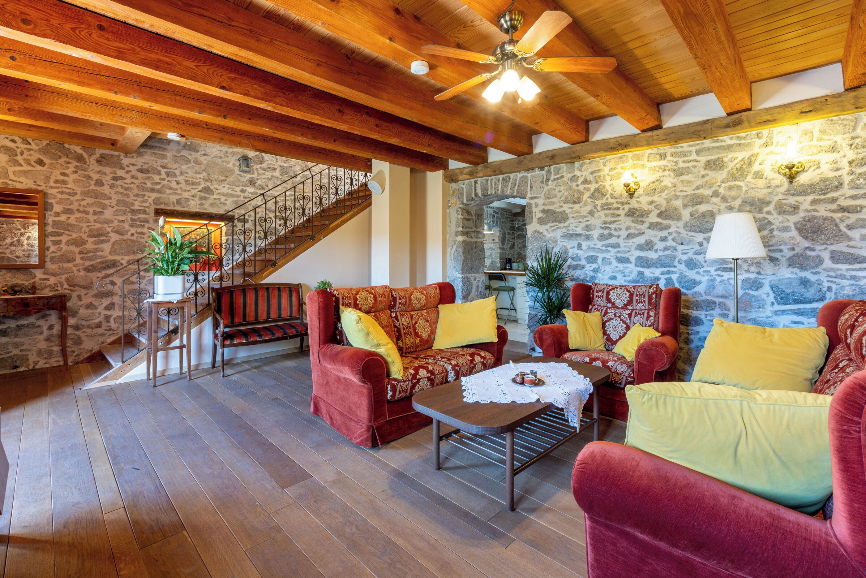 Un salon chaleureux avec un plancher en bois, des meubles rembourrés aux couleurs rouge et jaune, un mur en pierre et un escalier menant à un niveau supérieur.