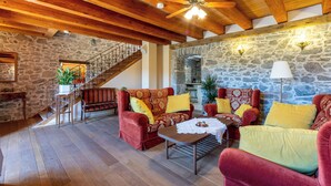 A cozy living room with wooden flooring, red and yellow upholstered furniture, a stone wall, and a staircase leading to an upper level. - House Carpe Diem (Jurdani)
