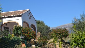 A white building with a tiled roof and arched doorways, surrounded by lush greenery and flowering plants. - Stay in Huetor, Rural Tourism in the Heart of Andalusia (Vinuela)