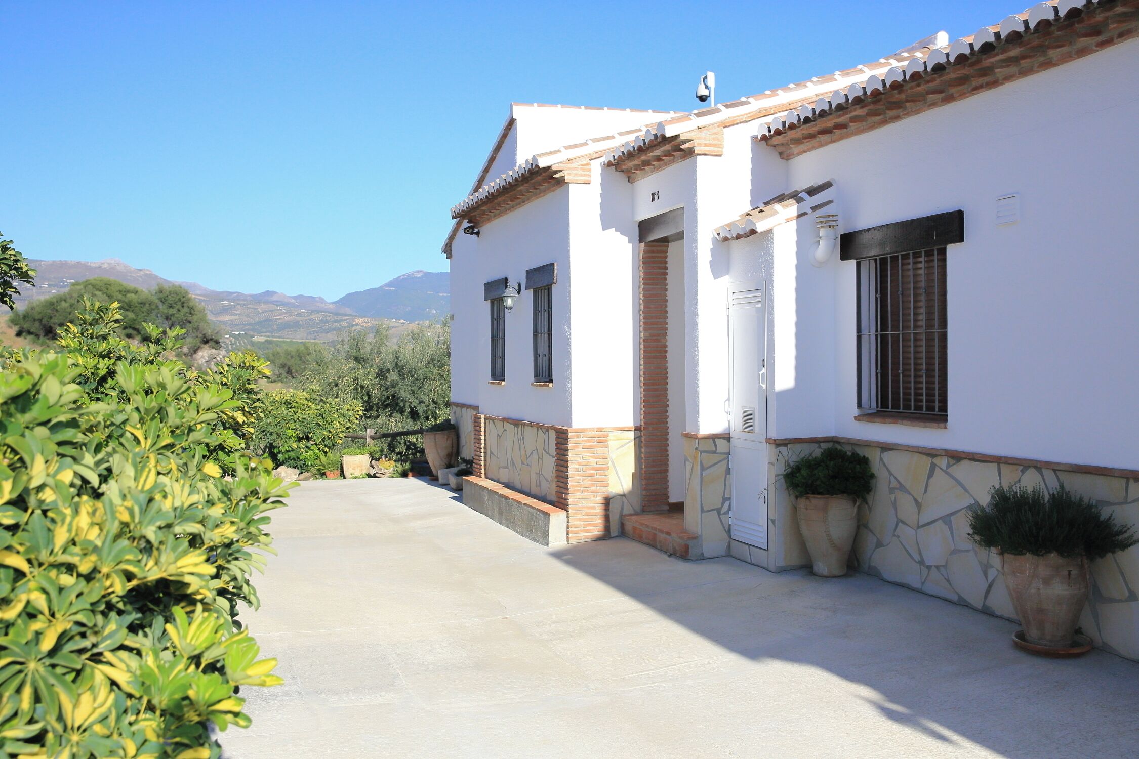 Un edificio blanco con techo de tejas, pared de piedra y un camino pavimentado.