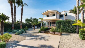 Una moderna casa a due piani con patio coperto, circondata da palme e curato giardino.