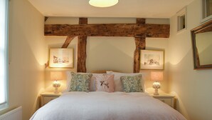 Une chambre avec un grand lit, des poutres apparentes, deux tables de chevet avec des lampes et des tableaux encadrés accrochés aux murs.