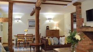 Un salon chaleureux avec des poutres apparentes, une cheminée, un canapé avec des coussins, une table à manger avec des chaises et un téléviseur fixé au mur.