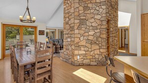 A spacious dining area with a stone accent wall, wooden furniture, and a chandelier. - Lassen Lane 15 (Bend)