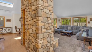 A spacious living area with a stone wall, a grey sectional sofa, a wooden coffee table, and a TV stand. - Lassen Lane 15 (Bend)
