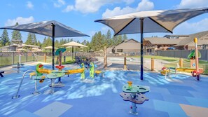 Children can play safely on the rubberized flooring, surrounded by swings, slides, and climbing frames under shaded umbrellas.