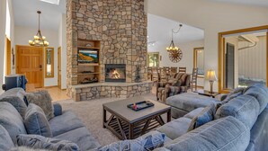 A living room with a stone fireplace, comfortable seating, and a television. - Lassen Lane 15 (Bend)