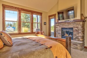 A bedroom with a large bed, a stone fireplace, and a TV mounted above it. - Pony Express Way 16795 (Bend)
