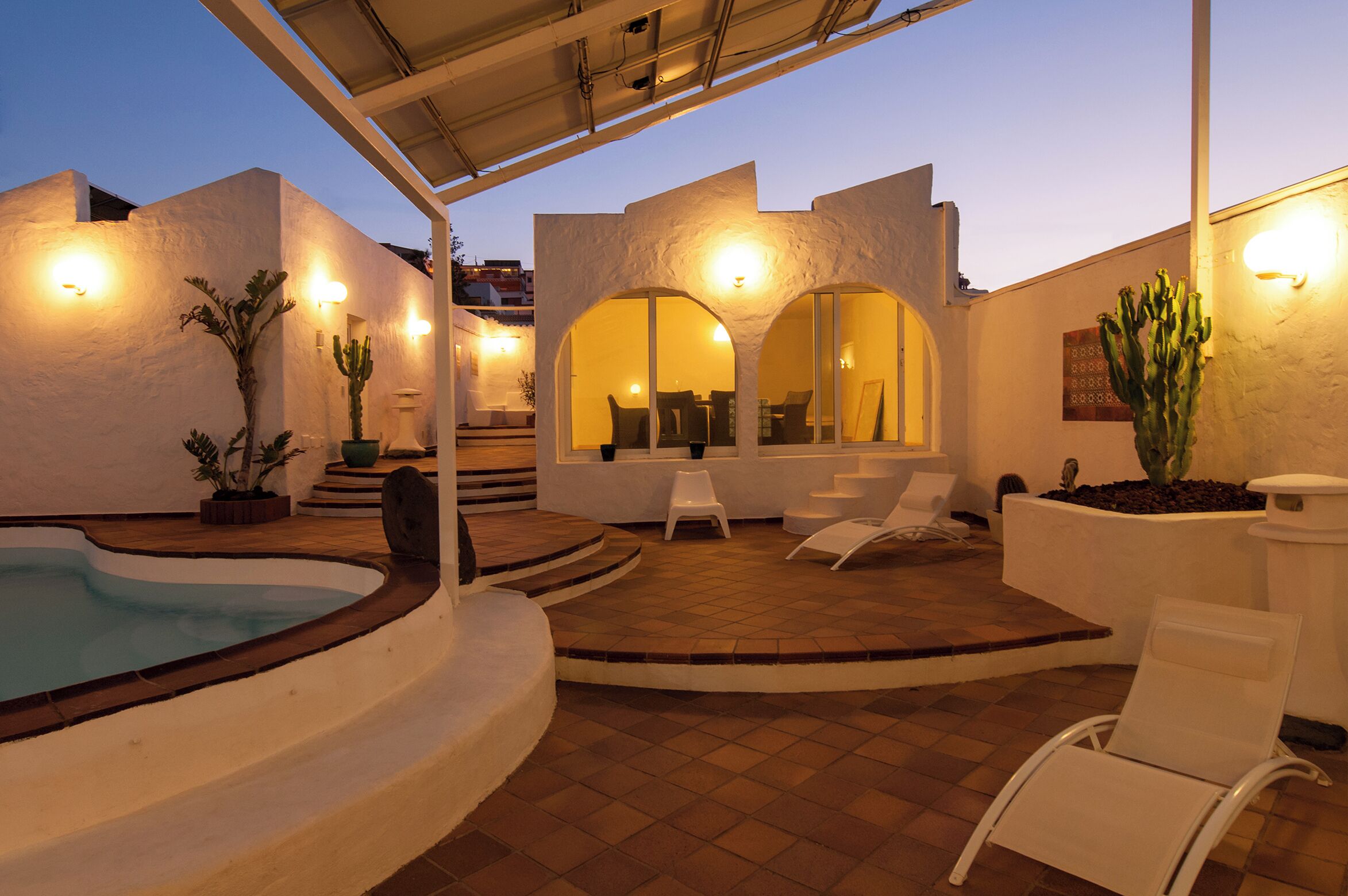 A modern outdoor patio with a swimming pool, white walls, and arched seating areas.