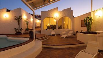 A modern outdoor patio with a swimming pool, white walls, and arched seating areas.
