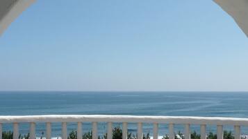 A coastal view through an arched window with a white railing, overlooking the sea.