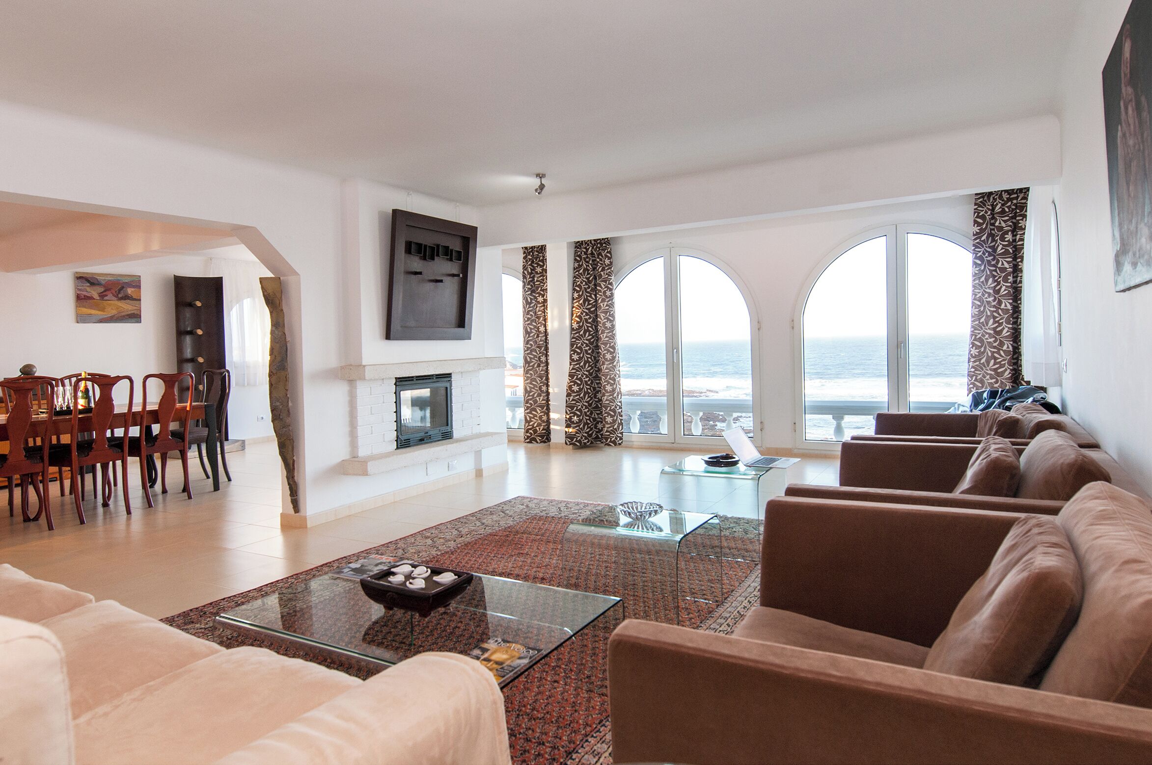 A spacious living area with a fireplace, a dining set, and a large window with a view of the sea.