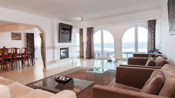 A spacious living area with a fireplace, a dining set, and a large window with a view of the sea.