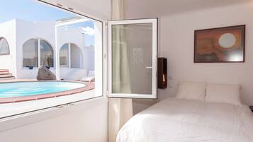 A bedroom with a bed, a painting, a view of a pool, and a white wall.