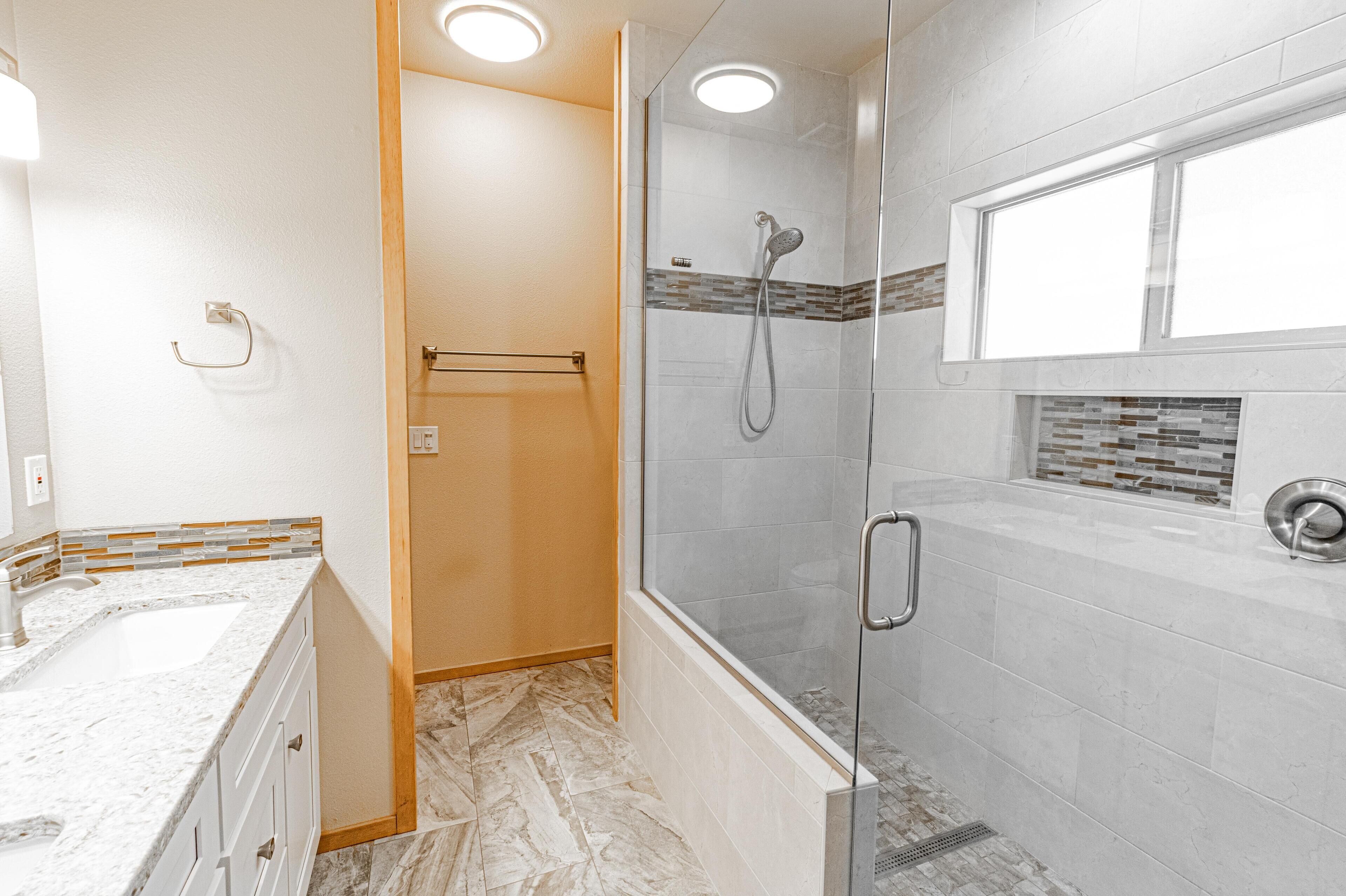 A modern bathroom with a glass-enclosed shower, a marble sink, and a tiled shower area.