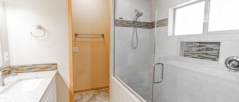 A modern bathroom with a glass-enclosed shower, a marble sink, and a tiled shower area.