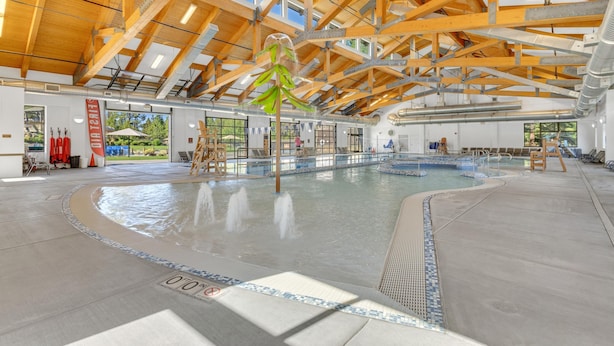 Une piscine intérieure dotée d’un plafond en bois, de murs en verre transparent et d’un sol carrelé.