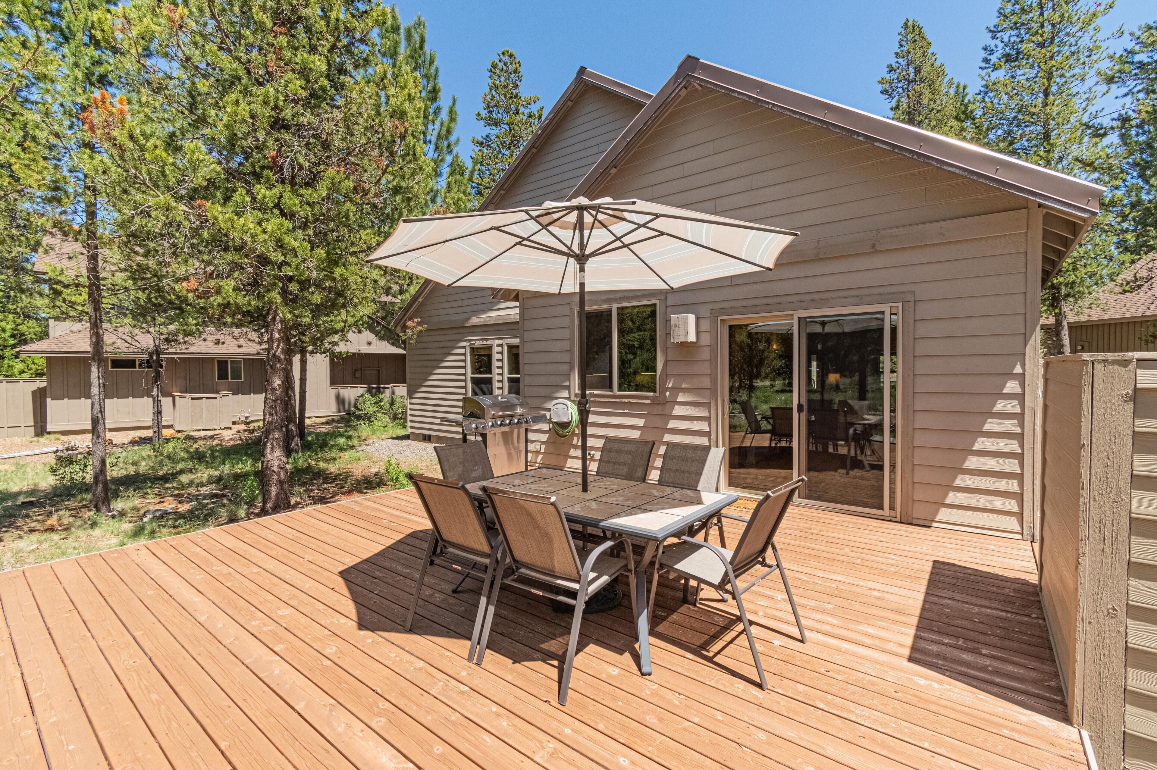 A wooden deck with a table and chairs, an umbrella, and a grill area.