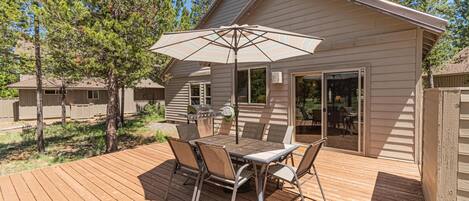 A wooden deck with a table and chairs, an umbrella, and a grill area.