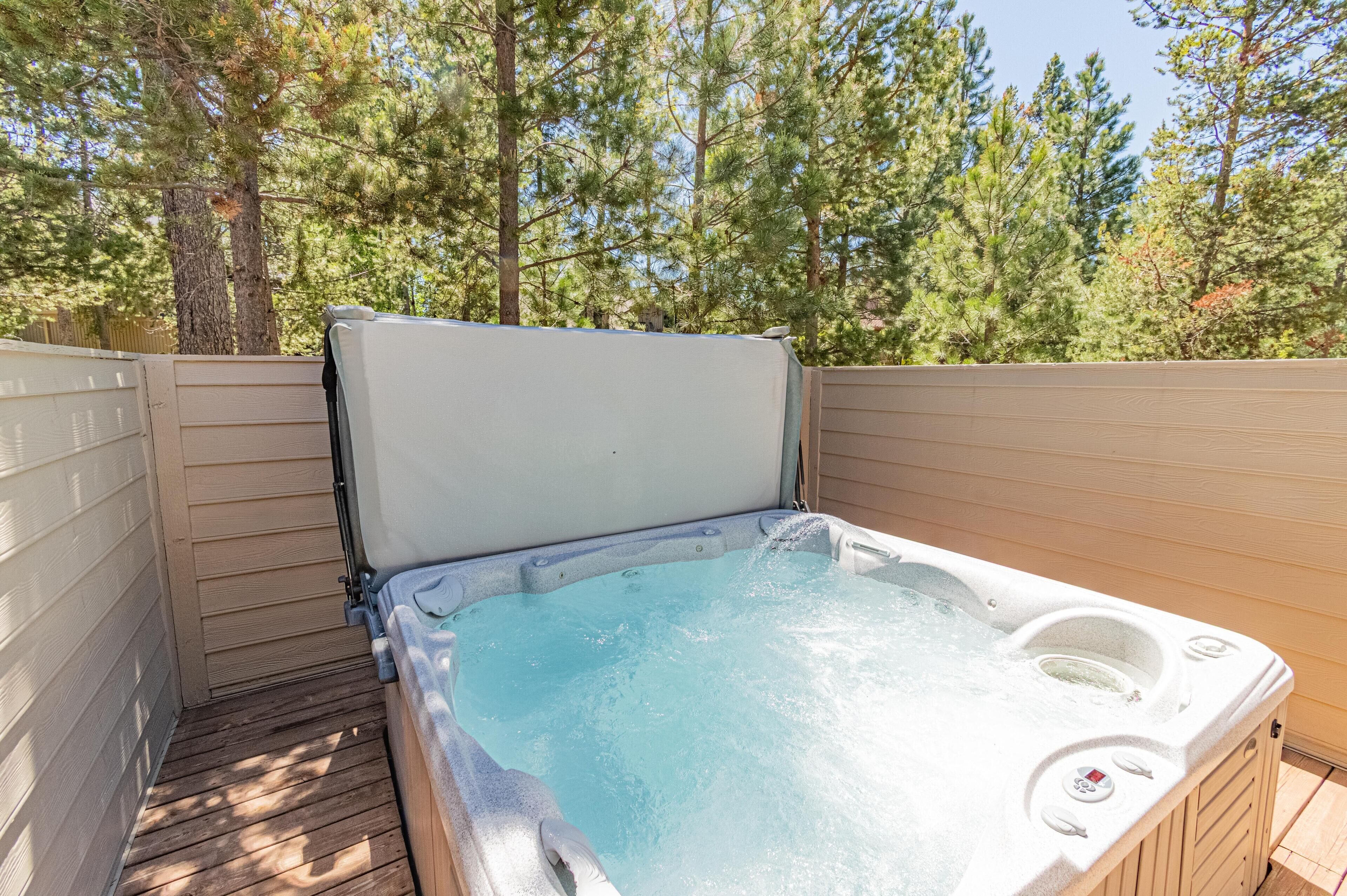 A hot tub with a wooden deck, surrounded by trees.