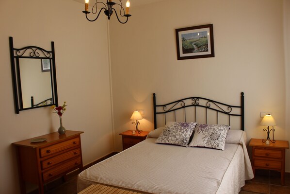 A bedroom with a bed, two bedside tables with lamps, a dresser, a mirror, and a framed picture on the wall. - House in Huetor, Perfect for Rural Tourism in Andalusia Spain (Vinuela)