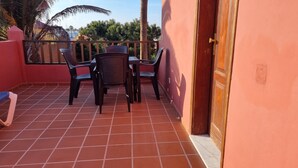 A balcony with a tiled floor, two wicker chairs, a table, and a door. - Nice Apartments With 3 Swimming Pools Wifi (La Oliva)