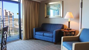 A hotel room with a blue sofa, a chair, a lamp, and a painting on the wall. - Caravelle Resort by Palmetto Vacations (Myrtle Beach)
