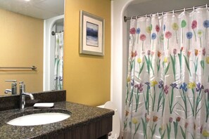 A bathroom with a granite countertop sink, a framed picture on the wall, and a shower curtain with a floral pattern.