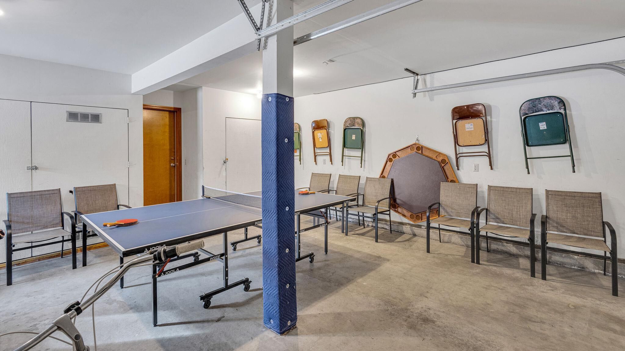 A spacious room with a ping pong table, several chairs, and a large mirror on the wall.