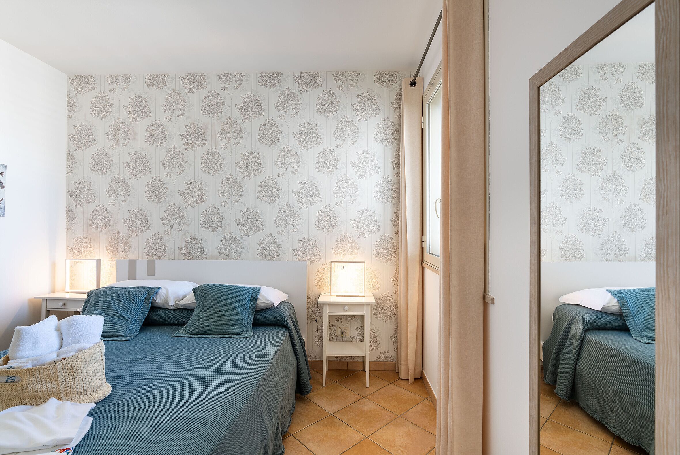 A bedroom with two beds, a bedside table with a lamp, and a mirror.