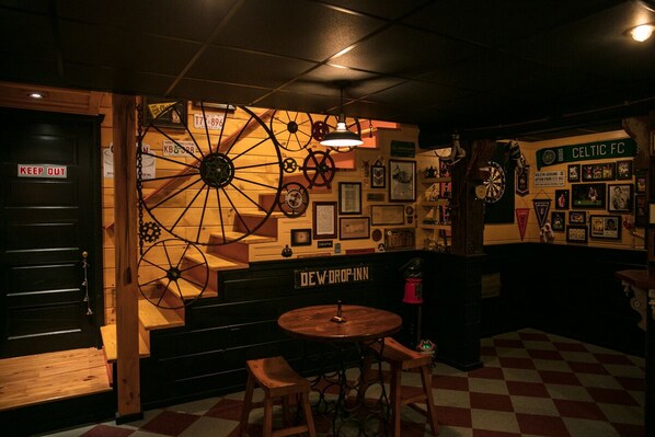 Un coin bar accueillant, avec une grande roue à aubes, des meubles en bois et des objets de collection accrochés aux murs.