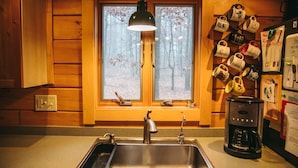 A kitchen with a double sink, a coffee maker, and a window with a view of trees. - Log Home in a Peaceful Wood in Jim Thorpe (Jim Thorpe)