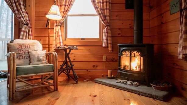 A cozy cabin interior with a wooden interior, a stone fireplace, a rocking chair, and plaid curtains. - Log Home in a Peaceful Wood in Jim Thorpe (Jim Thorpe)
