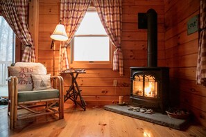 L’intérieur chaleureux d’un chalet, avec un décor en bois, une cheminée en pierre, un fauteuil à bascule et des rideaux à carreaux.