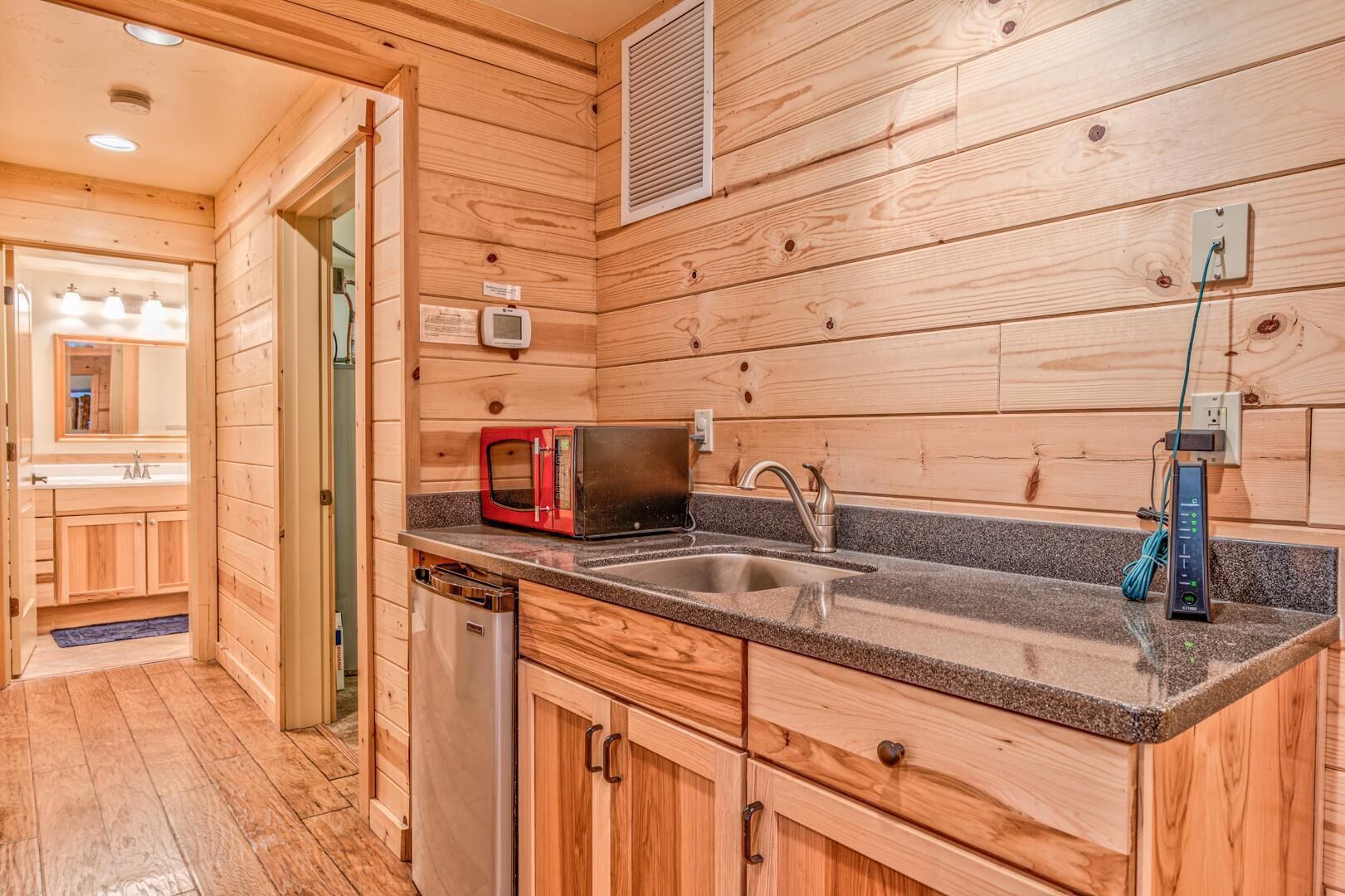 A compact kitchen with wooden walls, a granite countertop, a sink, a red microwave, and a dishwasher.