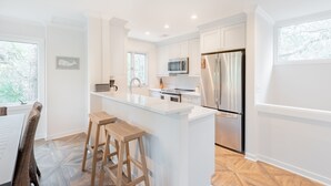 Una cocina moderna con armarios blancos, electrodomésticos de acero inoxidable y una isla central con taburetes.