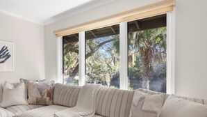 Un sofá de rayas beige con un plaid de punto, situado frente a una ventana con vistas a palmeras y follaje.