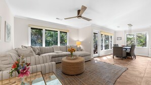Un salón espacioso con un sofá modular grande, un otoman redondo y un comedor con mesa y sillas.