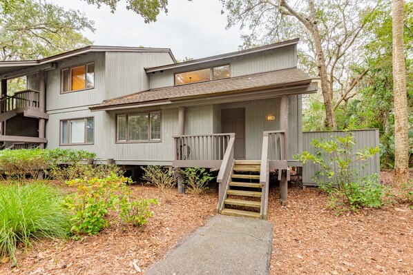 A two-story house with a front porch, wooden steps, and a small garden area.